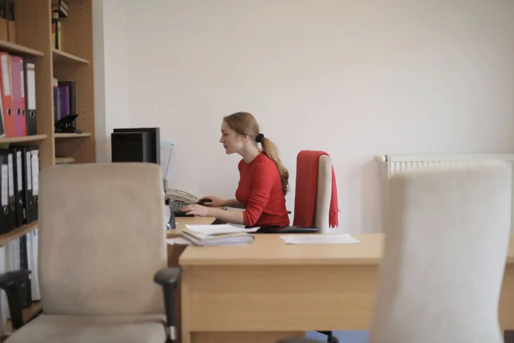 Woman sits at a desk working on a computer with head tilted forward